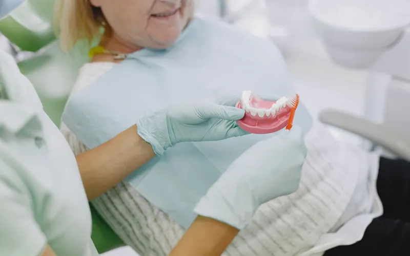 Profesional enseñando a una paciente mayor cómo cepillar la prótesis dental con ayuda de un modelo