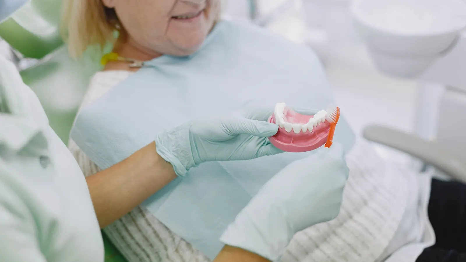 Profesional enseñando a una paciente mayor cómo cepillar la prótesis dental con ayuda de un modelo