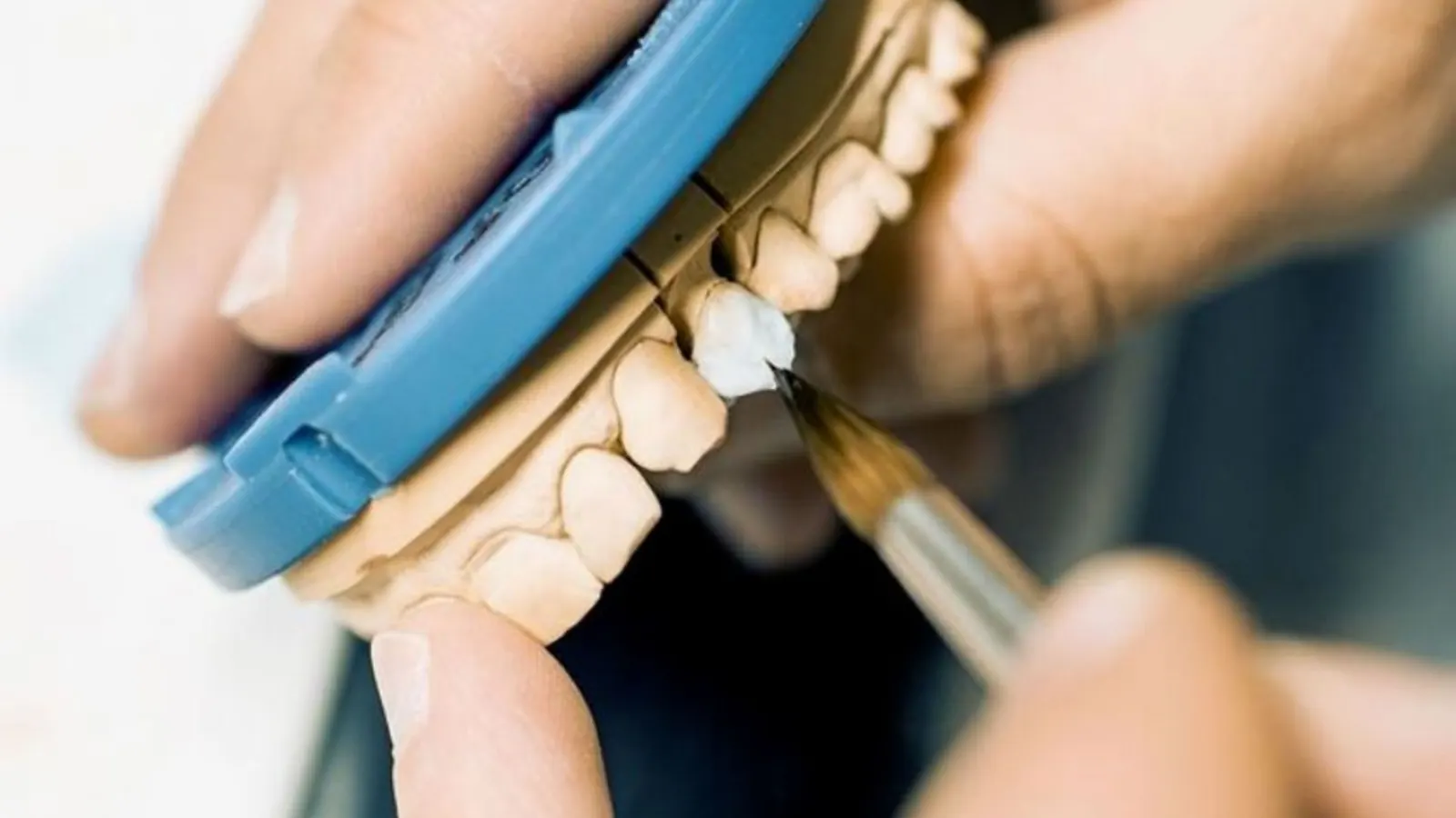Técnico dental maquillando con pincel unas coronas dentales de cerámica sobre el modelo