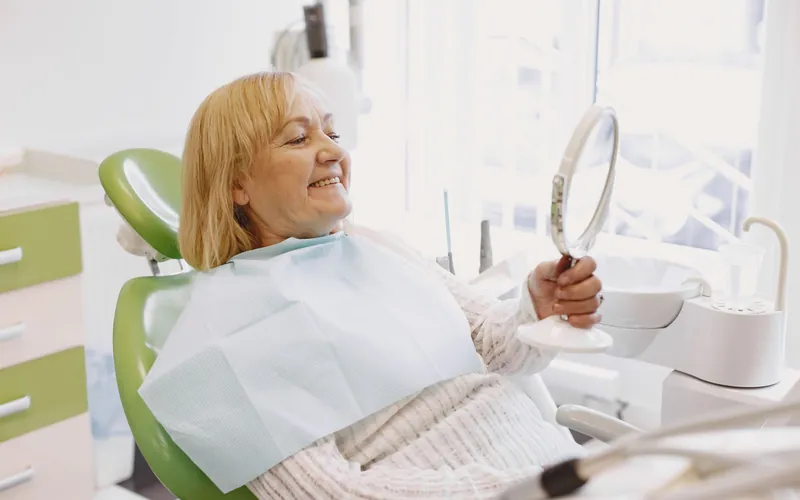 Paciente mayor sonriendo frente al espejo durante la revisión de su prótesis dental