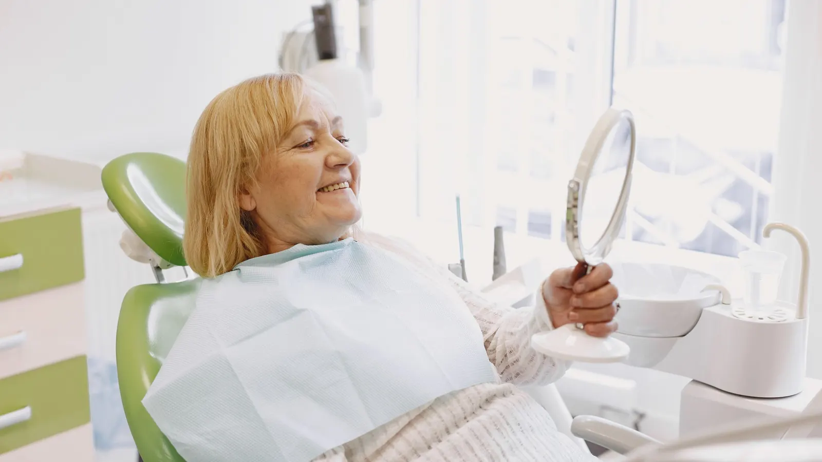 Paciente mayor sonriendo frente al espejo durante la revisión de su prótesis dental