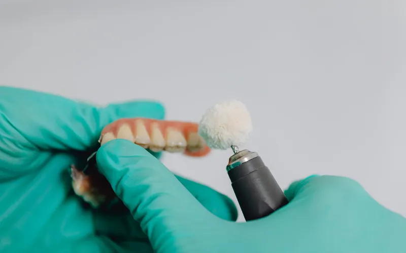 Técnico dental puliendo una dentadura postiza con un cepillo de fieltro en el laboratorio