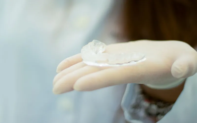 Férula de descarga transparente para el bruxismo sostenida con guantes en la clínica dental