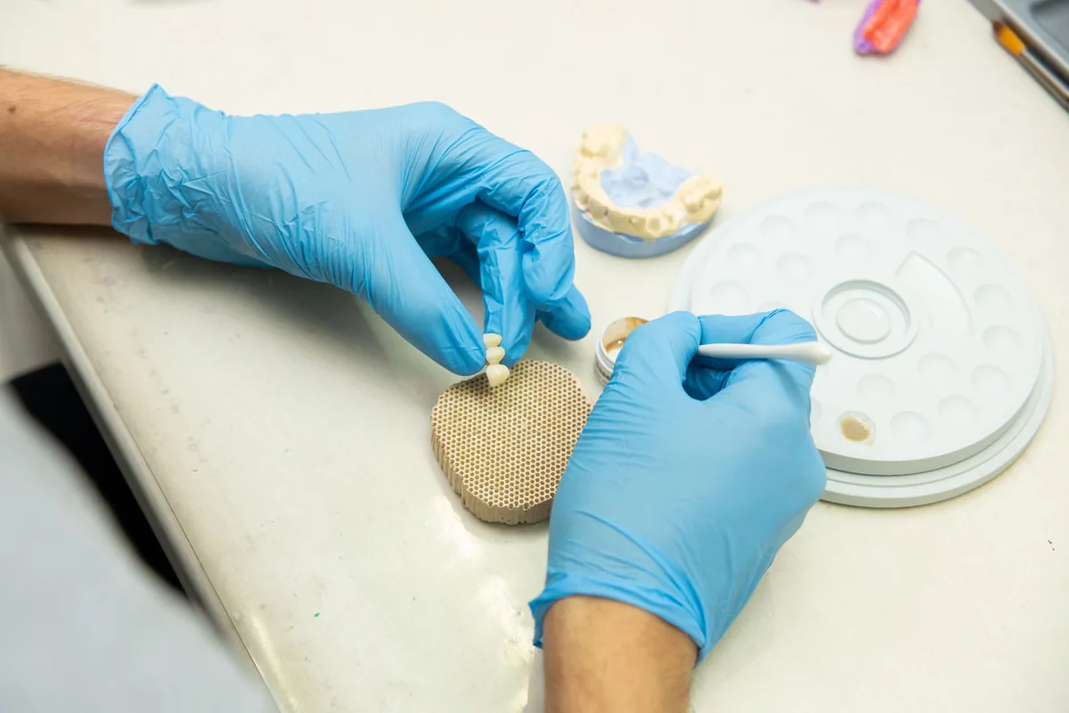 Manos de un técnico de laboratorio caracterizando una corona con pincel junto a la paleta de trabajo