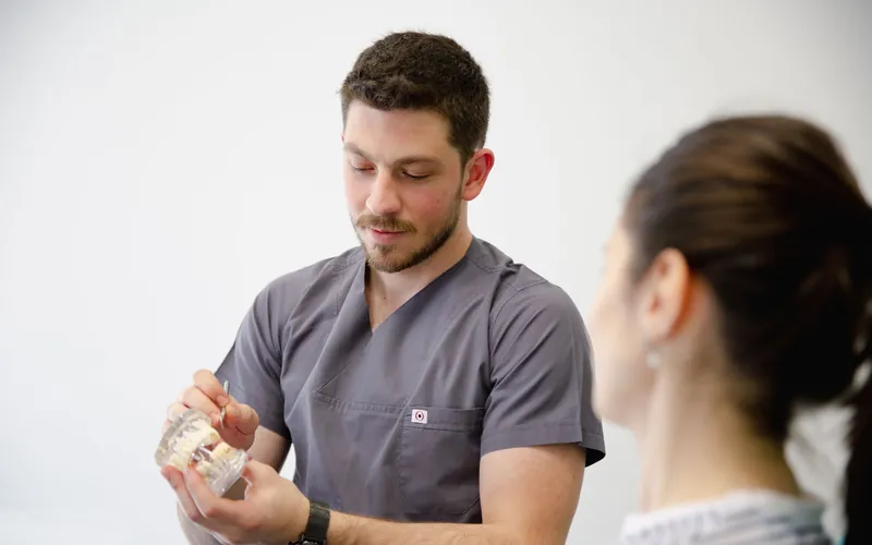 Dentista enseñando un modelo dental a una paciente para decidir entre prótesis dental fija o removible