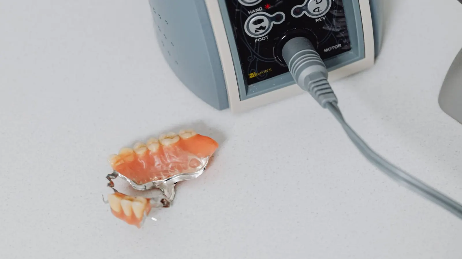 Prótesis esquelética removible con estructura metálica y dientes de resina junto al micromotor del laboratorio