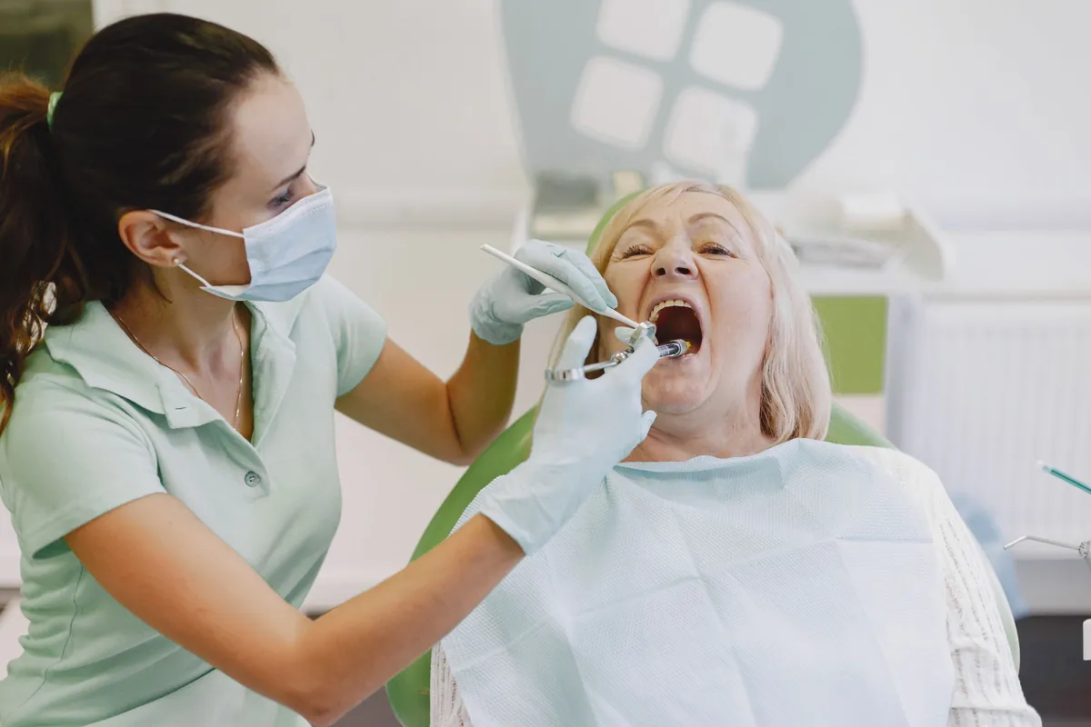 Dentista revisando la boca de una paciente mayor para comprobar si su prótesis necesita un rebase