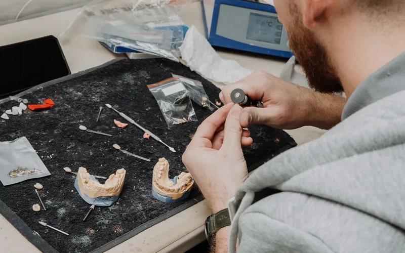 Técnico de laboratorio trabajando sobre una prótesis dental y sus modelos durante un rebase