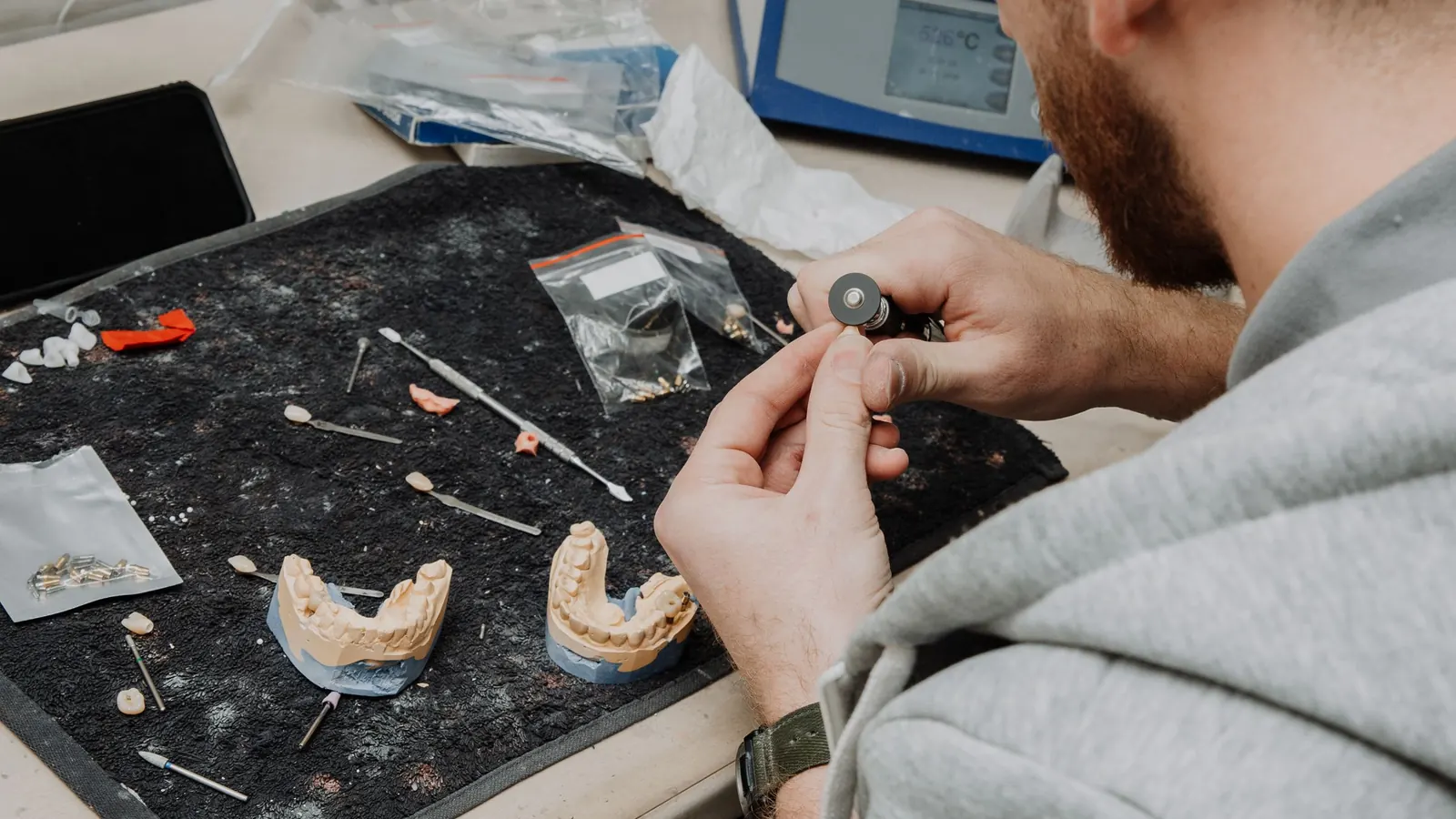Técnico de laboratorio trabajando sobre una prótesis dental y sus modelos durante un rebase
