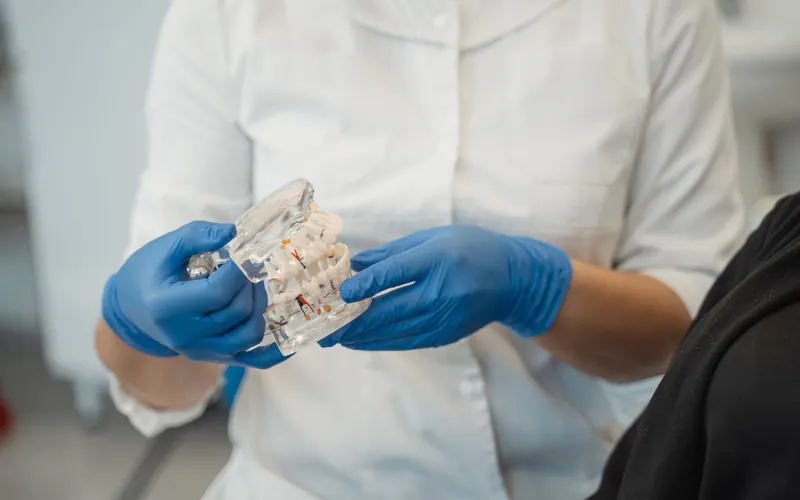 Dentista mostrando en un modelo transparente los implantes que sujetan una sobredentadura