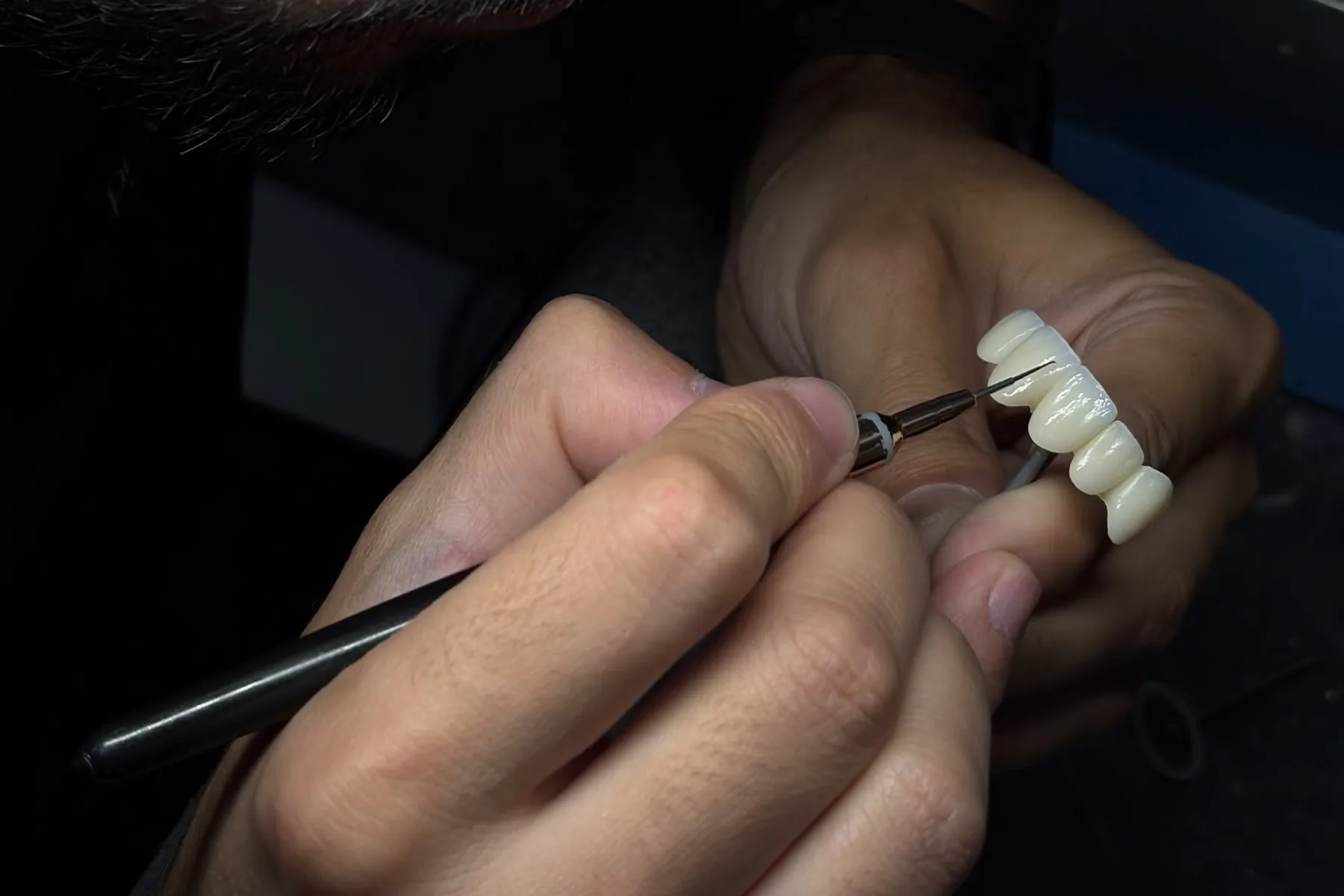 Manos de un técnico del laboratorio protésico dental trabajando a pincel un puente de varias piezas